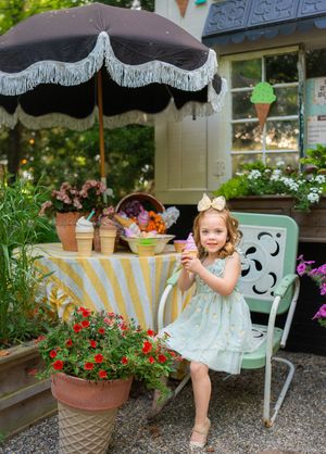 Mint green dress and garden bench surrounded by blooming flowers and decorative umbrellas in an outdoor setting.