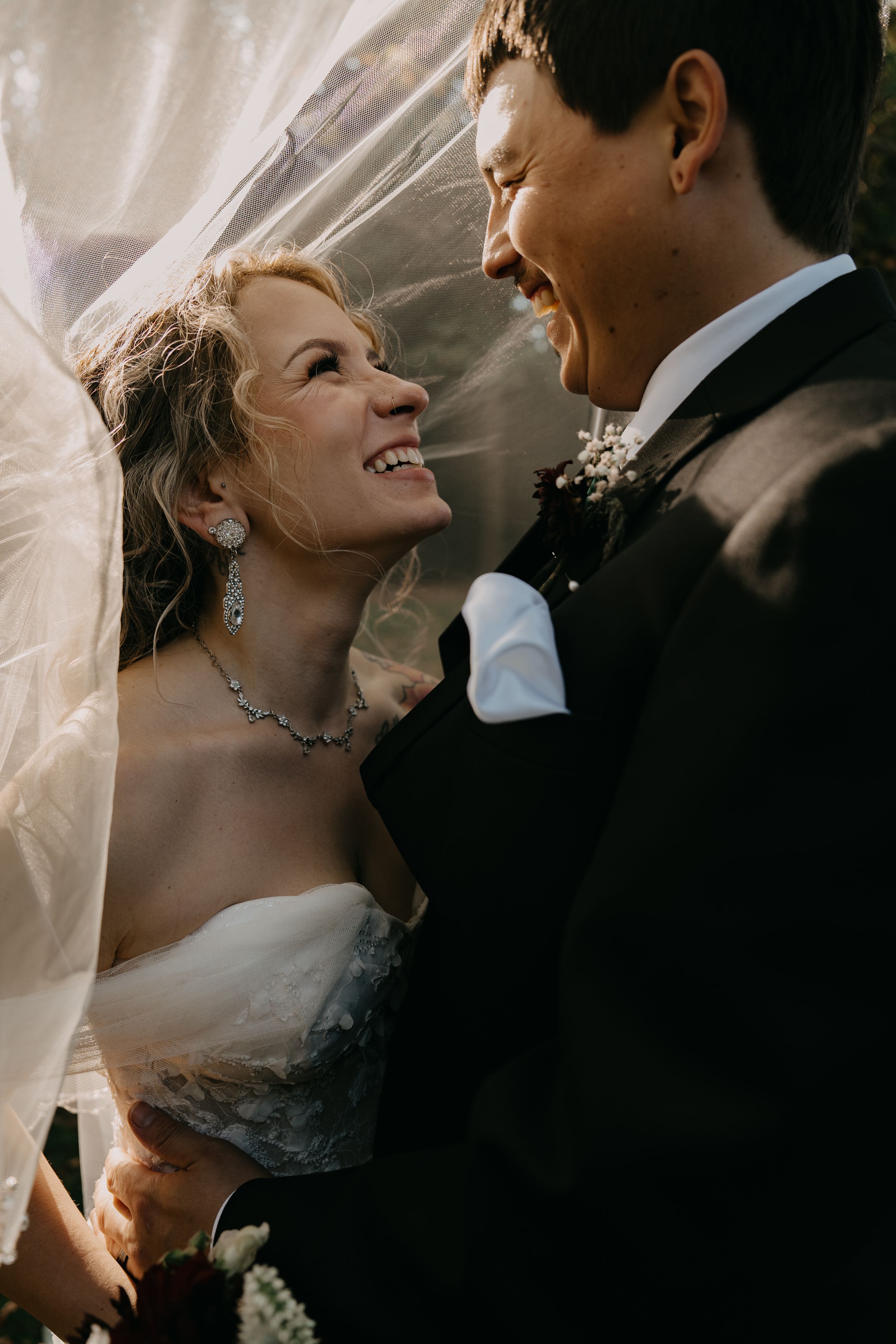 A joyful wedding moment captured between newlyweds sharing laughter under a flowing white veil.