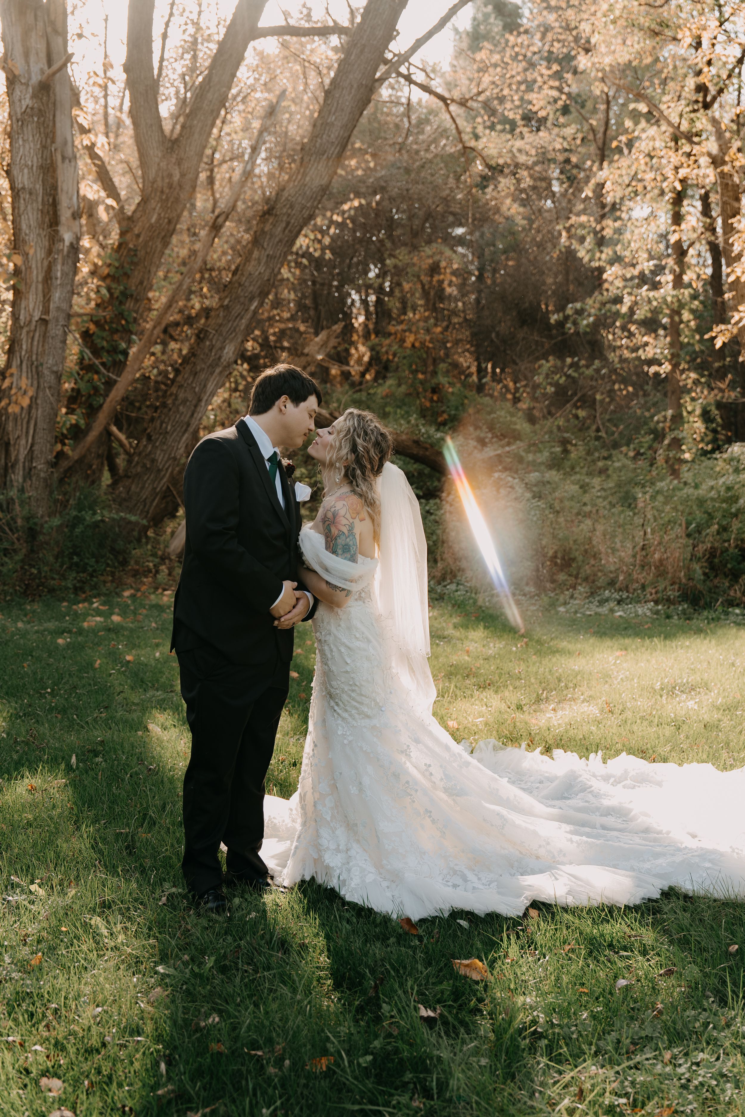 Wedding couple poses together in a dreamy autumn woodland setting with sunlit trees in the background.