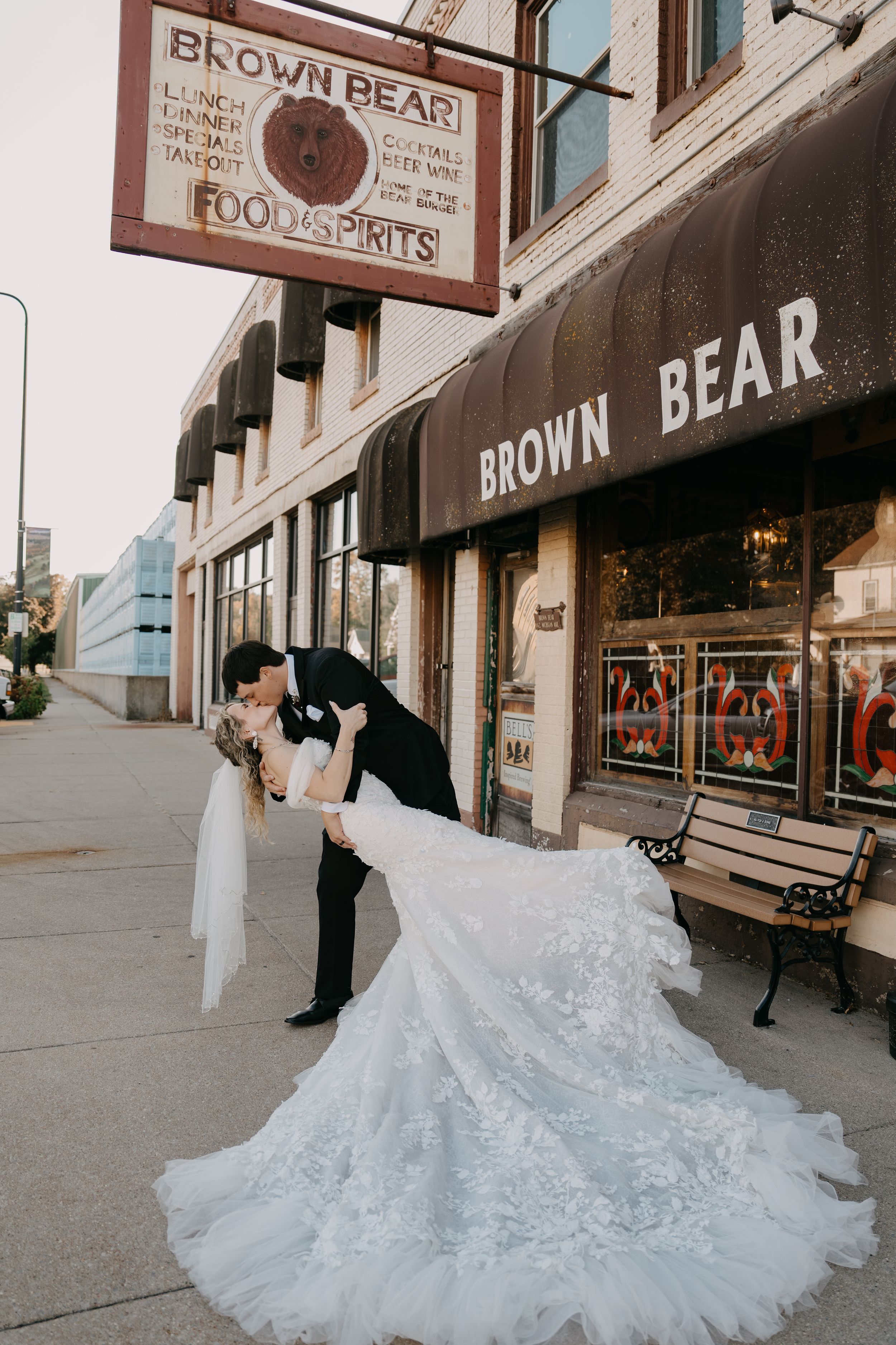Dramatic wedding photo of a couple's dip kiss outside Brown Bear storefront with bride's flowing dress train.