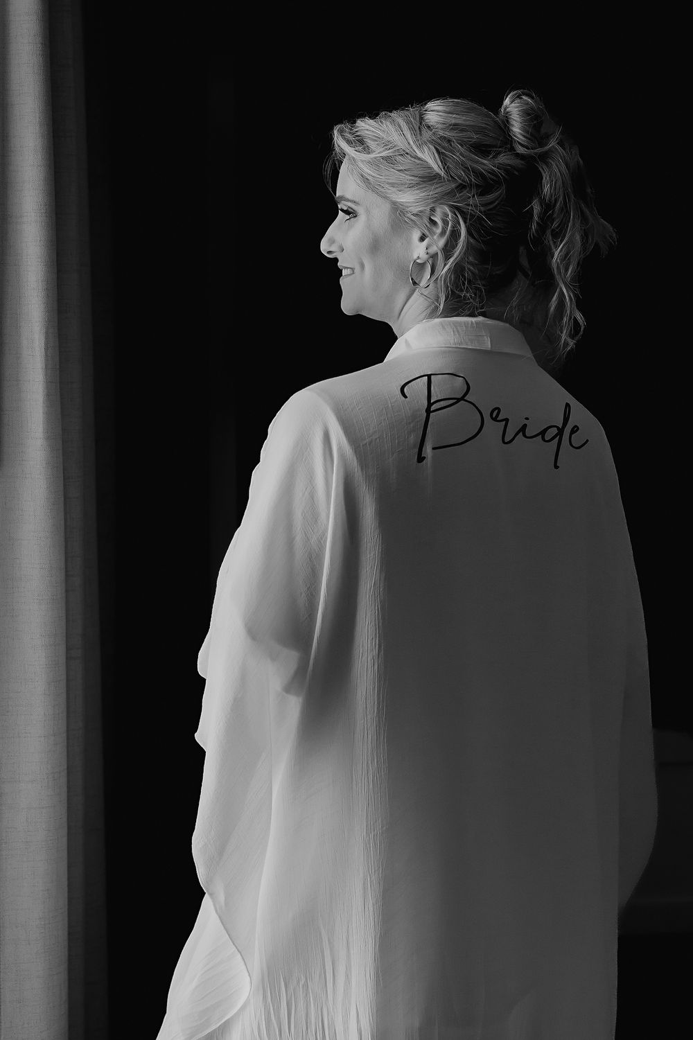 A black and white portrait showing the back of a robe with 'Bride' written on it while getting ready for a wedding.