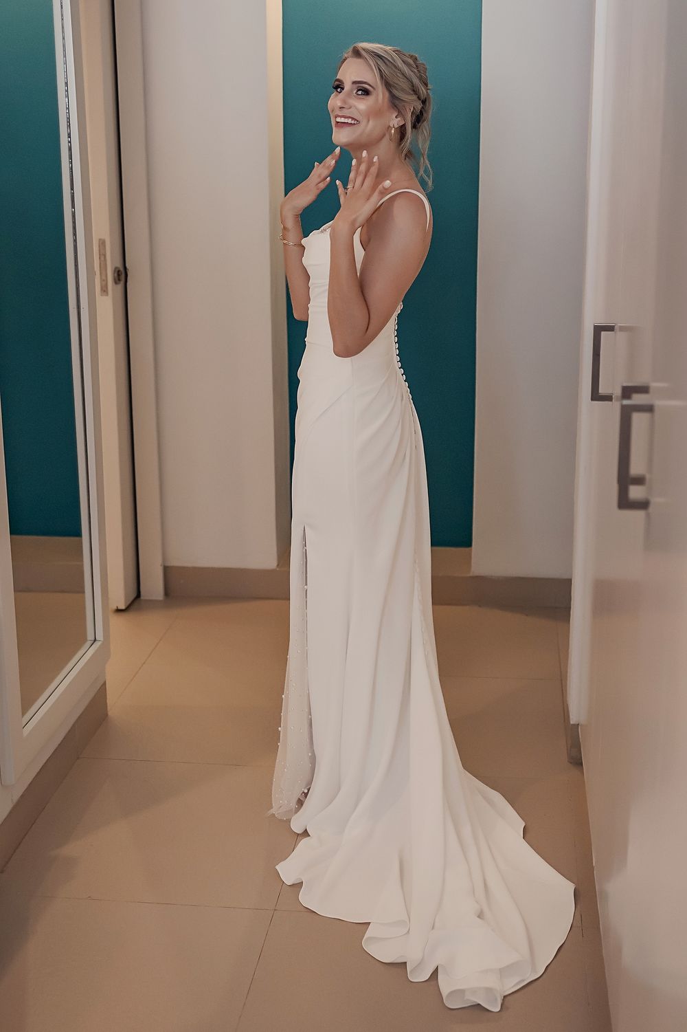 A sleek white wedding dress with an elegant open back design and flowing train shown in a fitting room.