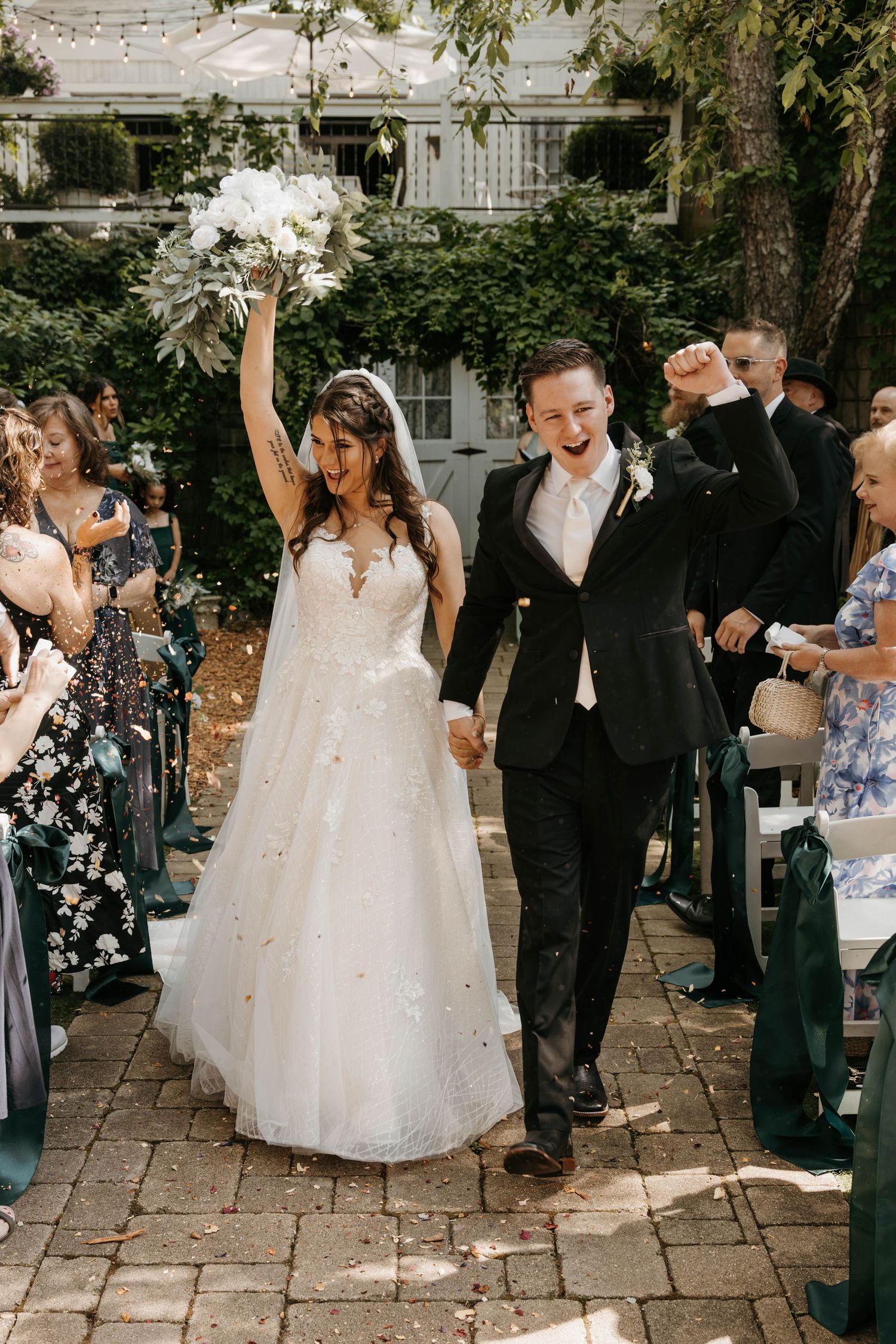 Joyful bride and groom celebrating recessional walk with guests cheering and tossing confetti outdoors.