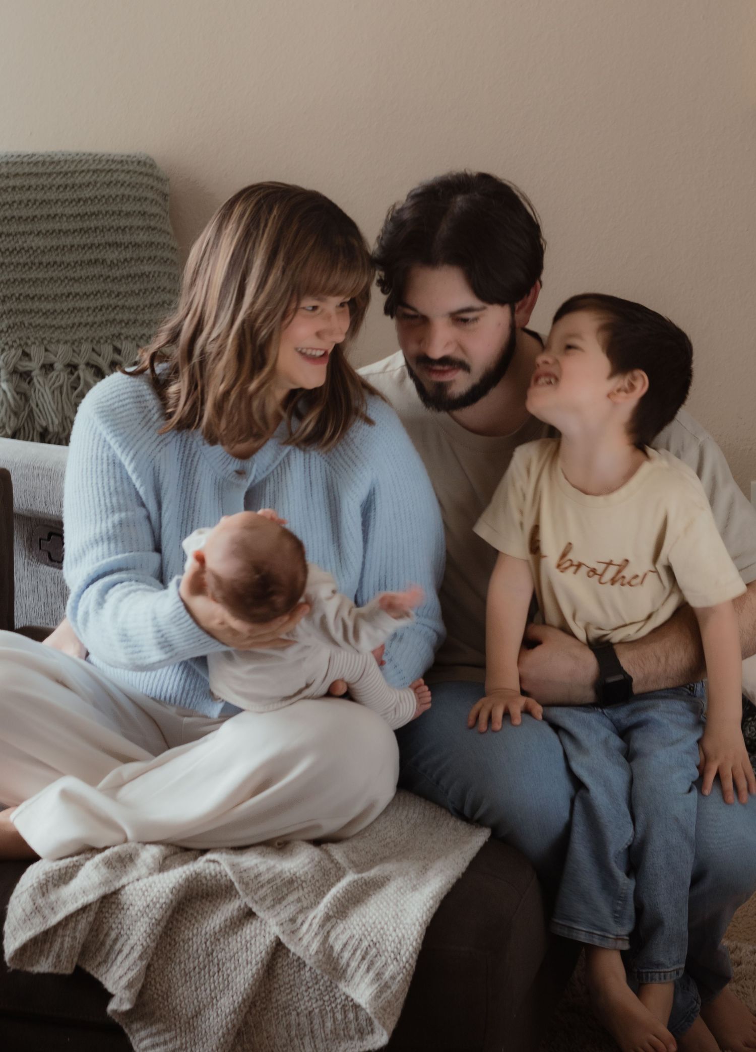 In-home family photo of parents cuddling with their newborn and toddler during a cozy lifestyle session in Kennewick WA