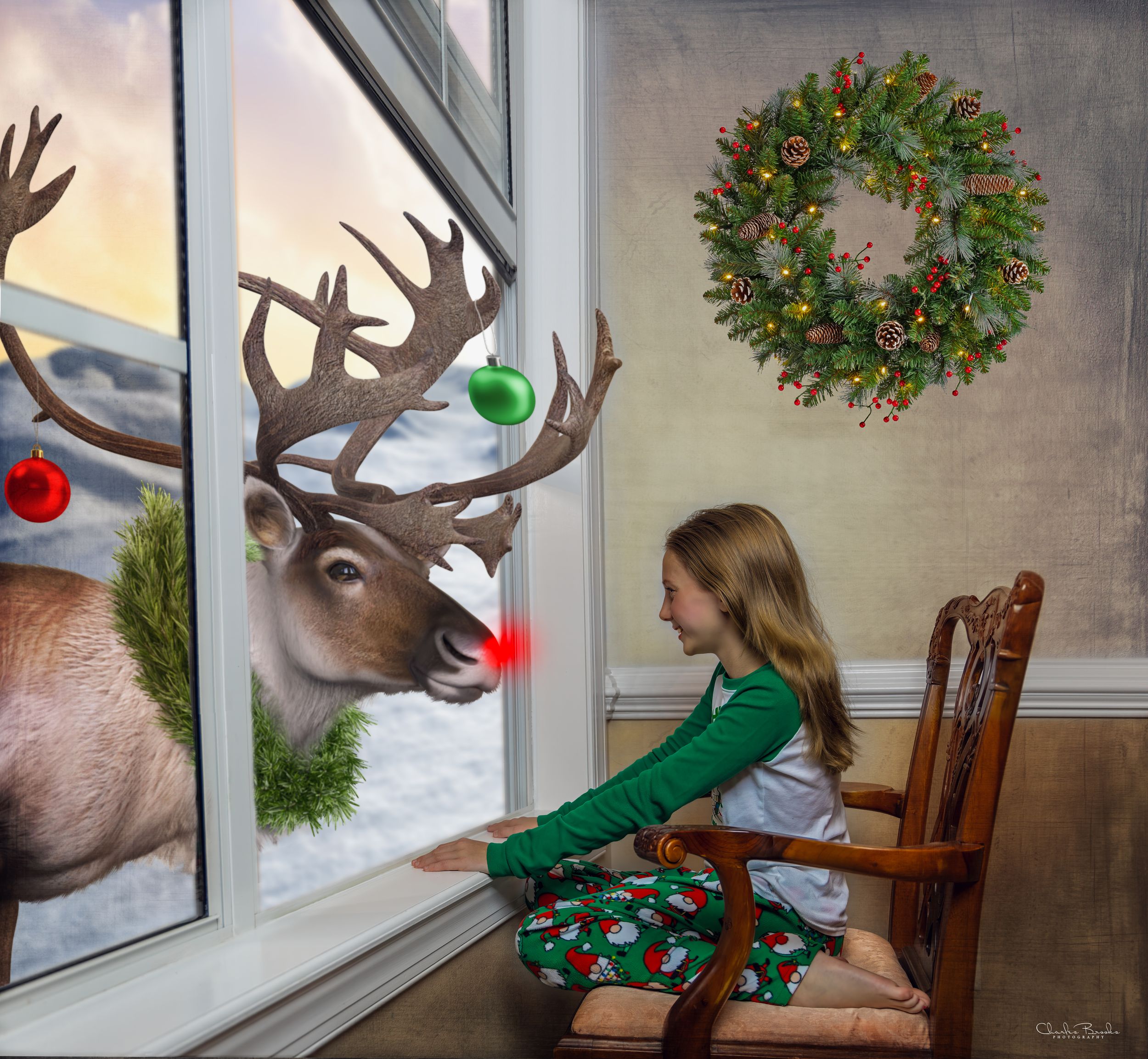 Child in green dress looks at reindeer decoration through window with Christmas wreath hanging.