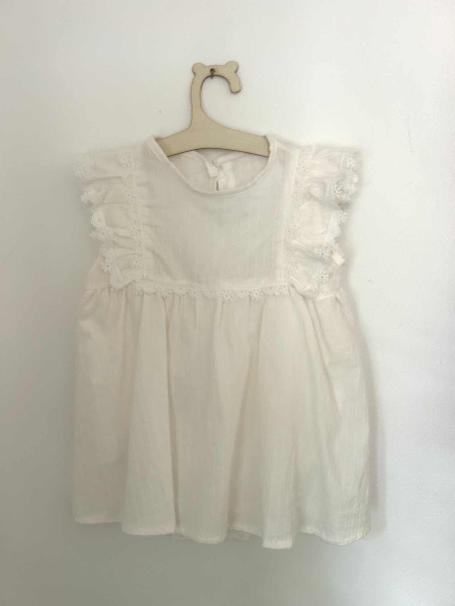 Vintage-style beige knitted baby romper with button details and side pockets hanging on display.