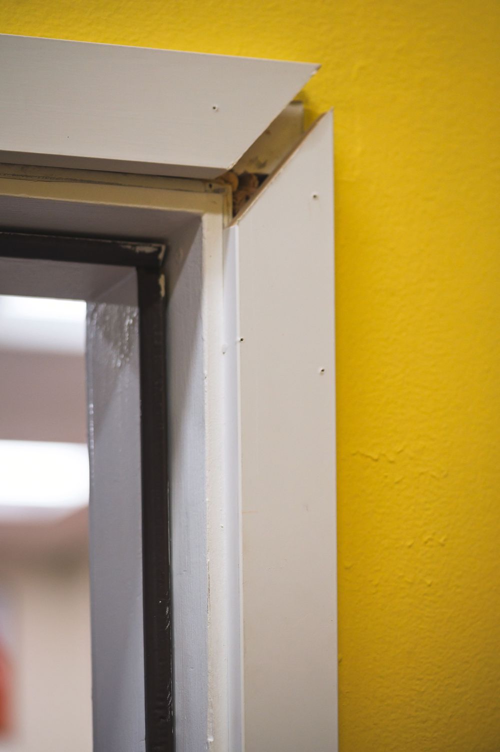 Door frame detail showing white trim against bright yellow wall with partial view of doorway.
