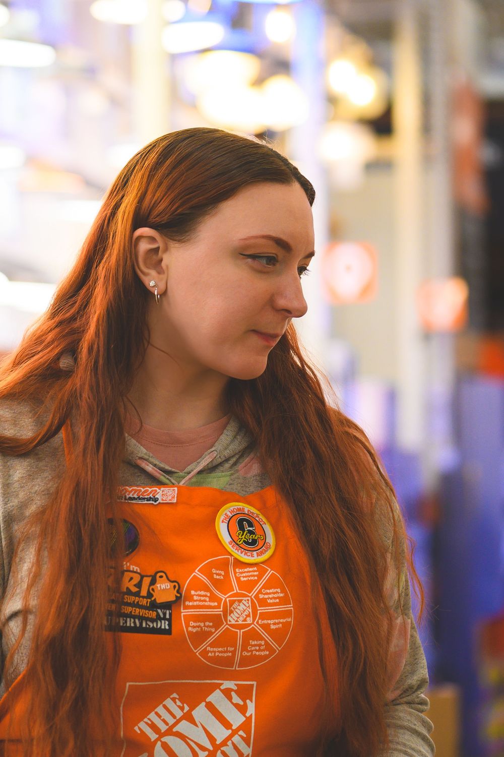 Side profile view of someone wearing an orange t-shirt with light-colored long hair against a blurred background.