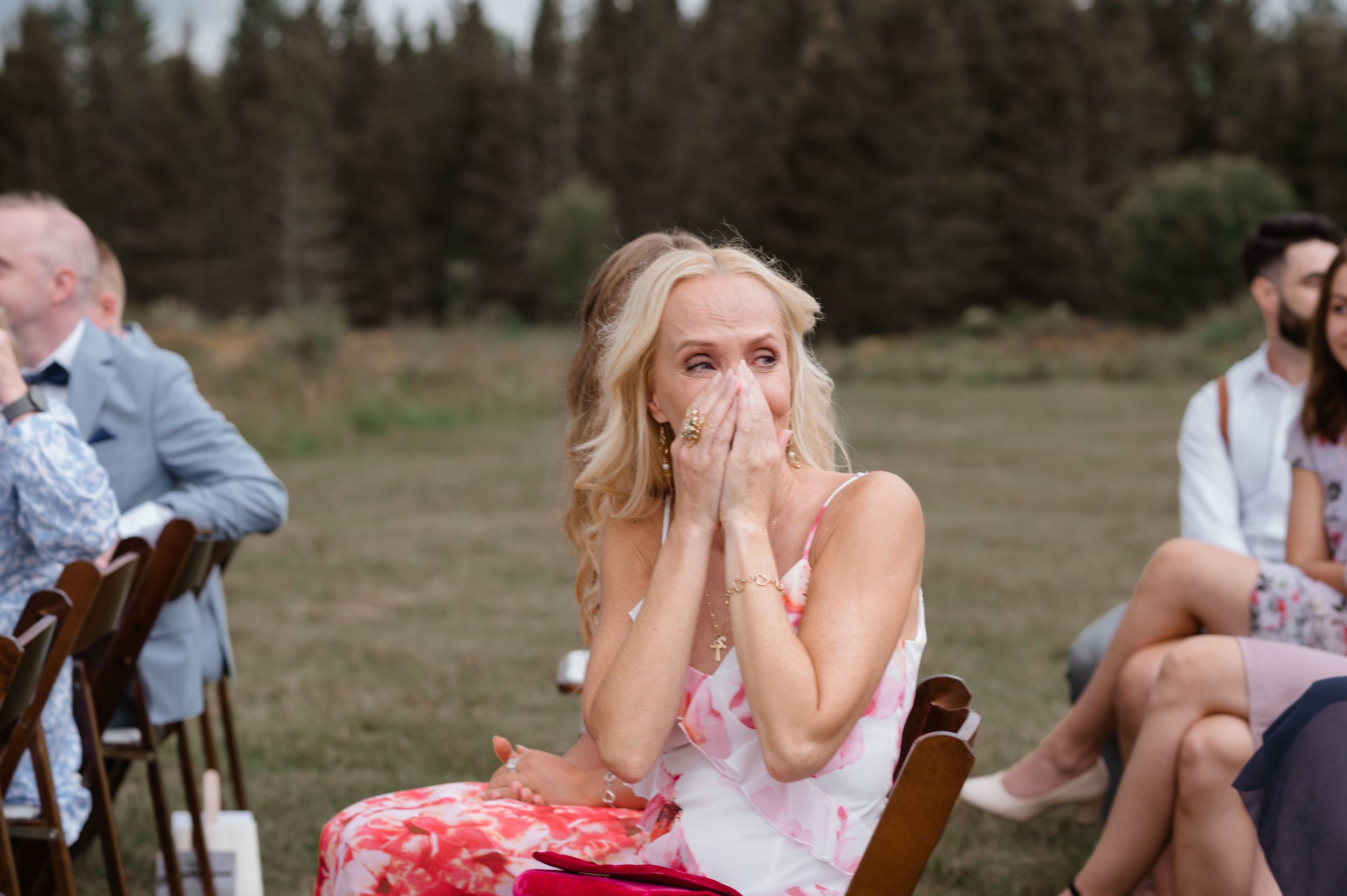 Someone in colorful attire displays an emotional reaction during an outdoor wedding ceremony with forest backdrop.