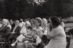 A black and white photo shows guests seated outdoors at what appears to be a special event or wedding ceremony.
