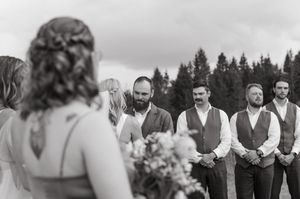 An exchange of heartfelt glances during an outdoor wedding ceremony with evergreen trees in the background.