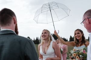 A joyful moment at an outdoor wedding ceremony with a clear umbrella being held up against an overcast sky.
