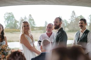 A happy couple stands at their wedding ceremony surrounded by the wedding party under a covered outdoor venue.