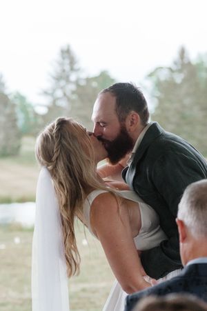 A romantic first kiss at a wedding ceremony with a flowing veil and scenic outdoor backdrop.