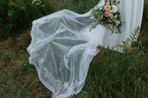 A flowing white wedding veil and floral bouquet against a natural outdoor background.