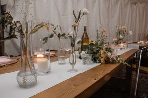 An elegant wedding reception table decorated with candles, glass vases, and natural floral arrangements on a white tablecloth.