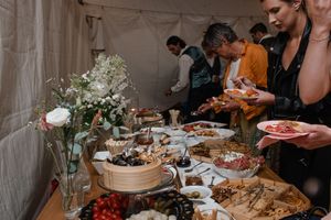 People gathering at a buffet table with assorted dishes, appetizers, and white flower arrangements at a catered event.
