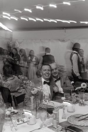 Black and white photograph of wedding reception guests seated at banquet tables with floral centerpieces and place settings.
