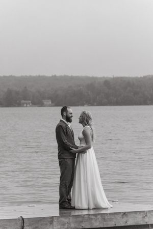 A romantic black and white lakeside scene with a couple embracing on a wooden dock with trees in the background.