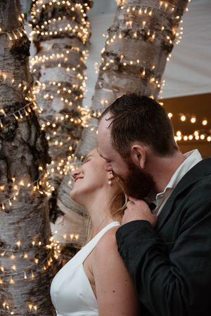 A romantic moment captured under twinkling tree lights during a wedding celebration.