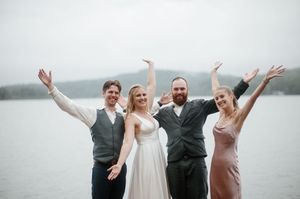 Wedding party celebrates with arms raised against a misty lake backdrop.