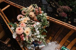 Gorgeous peach and pink floral wedding bouquet resting on rustic wooden benches.
