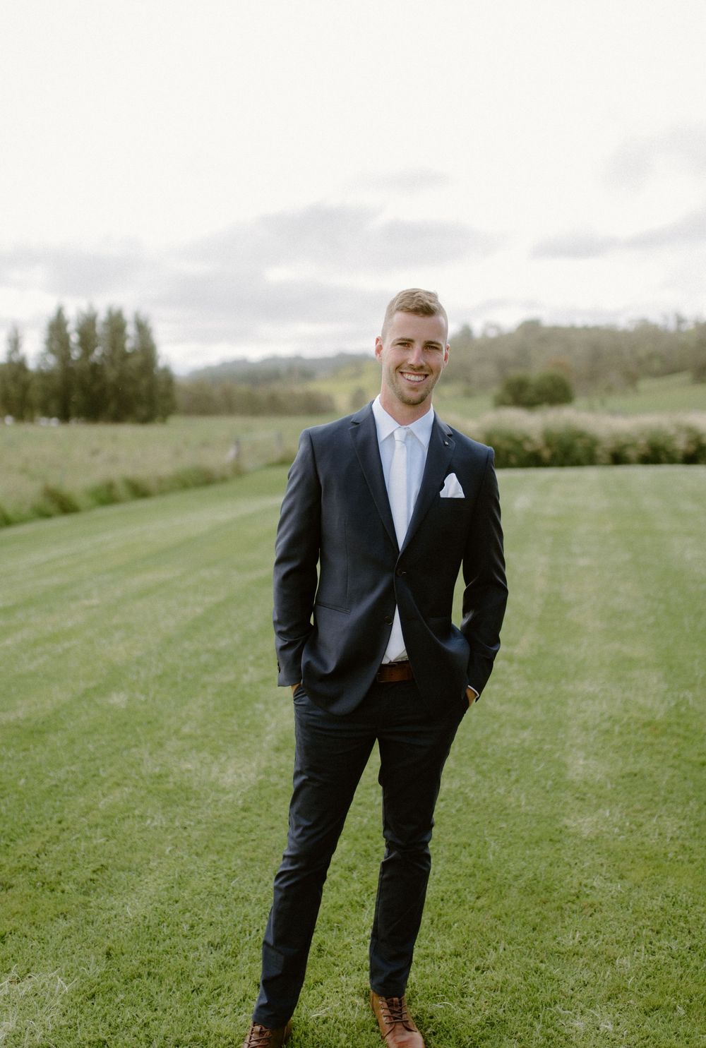 Classic groom portraits on a rolling green hillside in a navy suit.