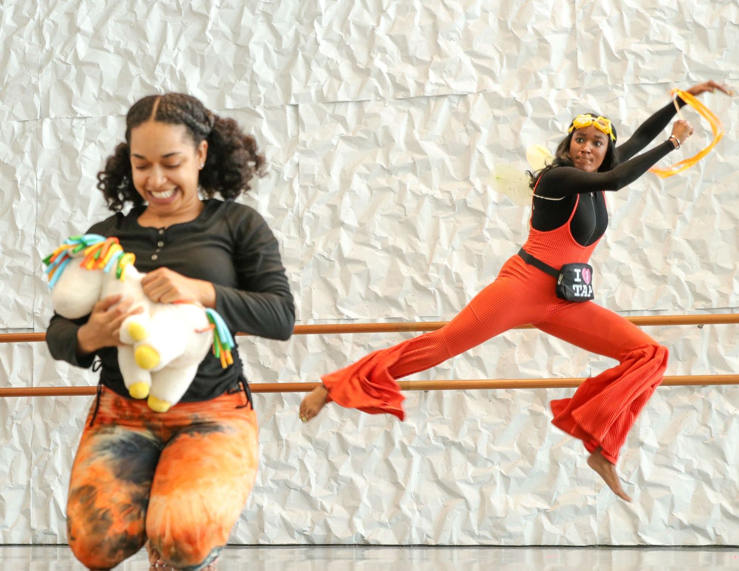 A series of dance movements shows a dramatic leap sequence with flowing orange fabric against a white textured wall.