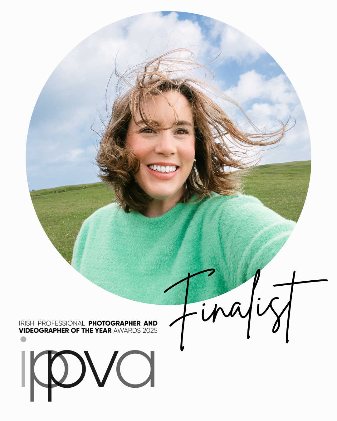 Casual outdoor portrait against green hillside with windswept hair and bright smile.