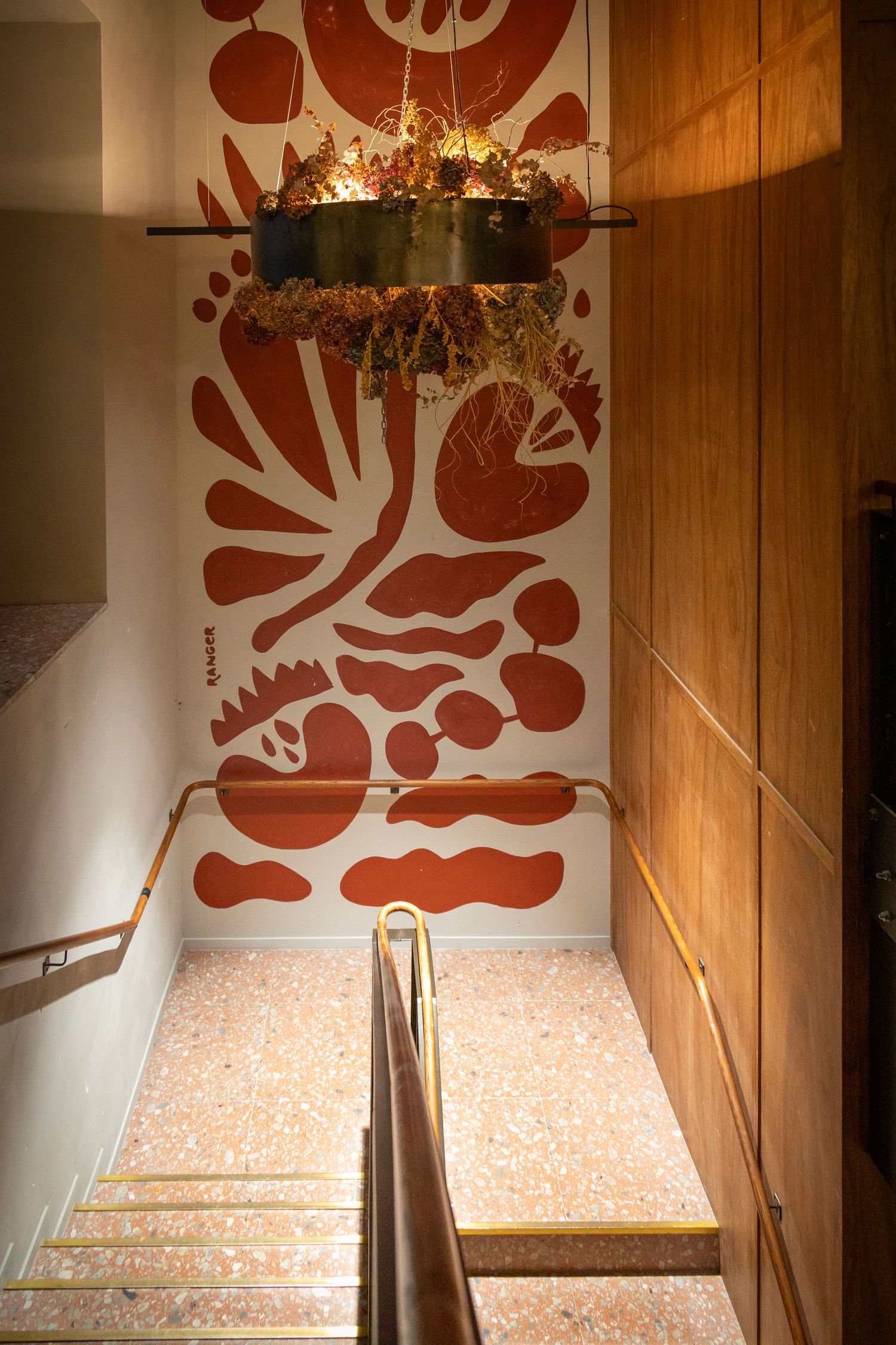 Stairwell with terrazzo floors, wooden walls, and bold botanical mural leading downward.