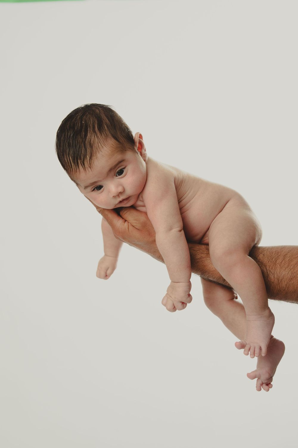 Newborn baby held securely in adult hands against white background, looking curiously at camera.