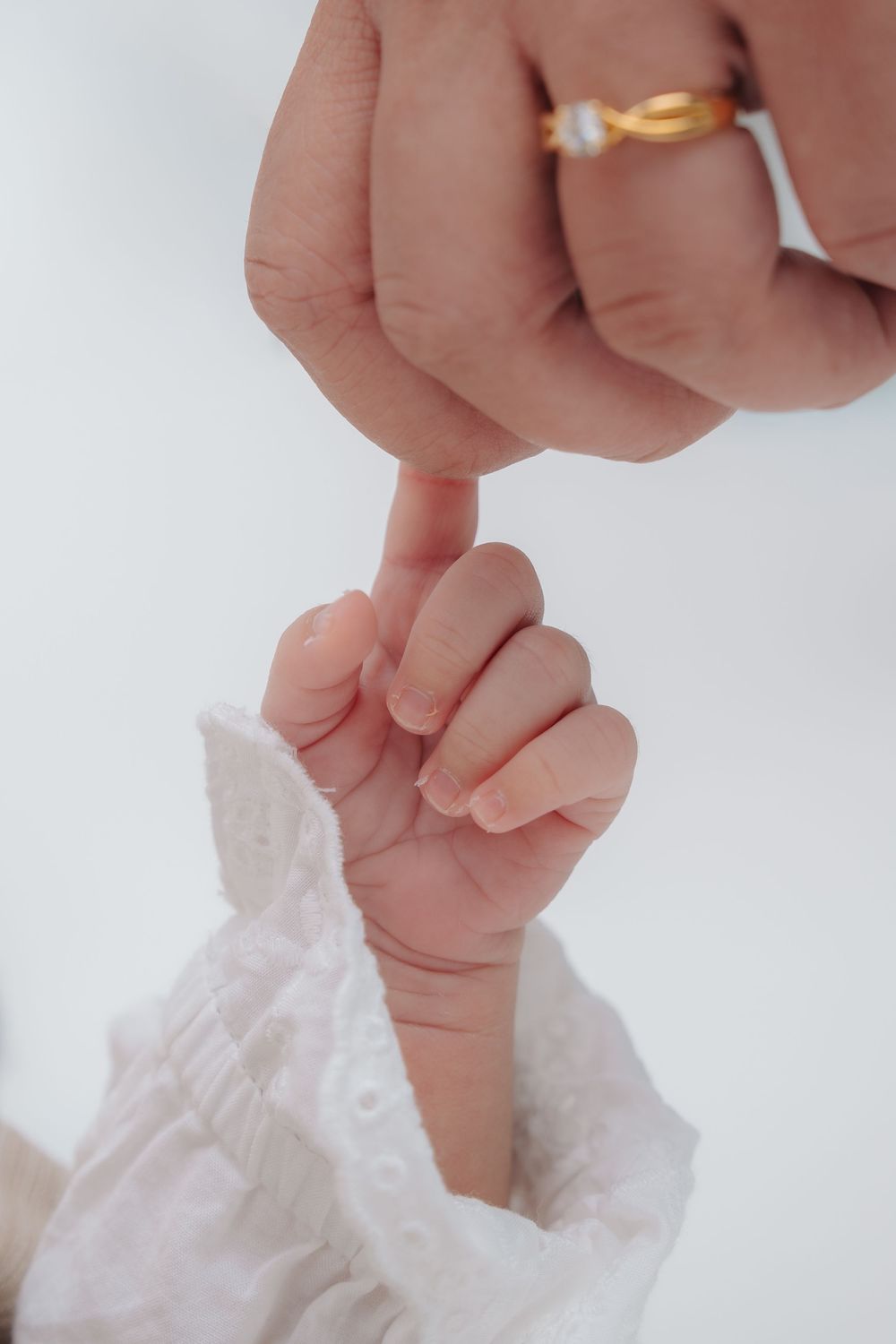 Close-up view of delicate baby hands reaching up against a white background with soft lighting.