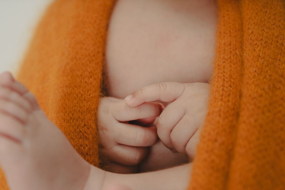 Close-up of a newborn baby's tiny hand peeking out from an orange knit blanket.