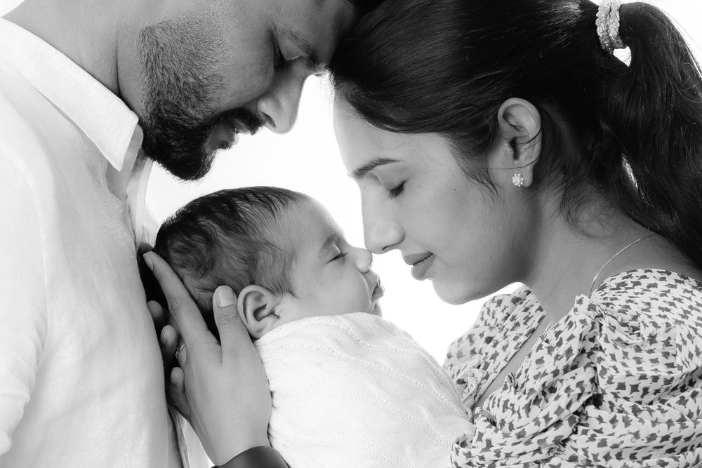 Black and white photo of parents tenderly holding their newborn baby close, sharing an intimate family moment.