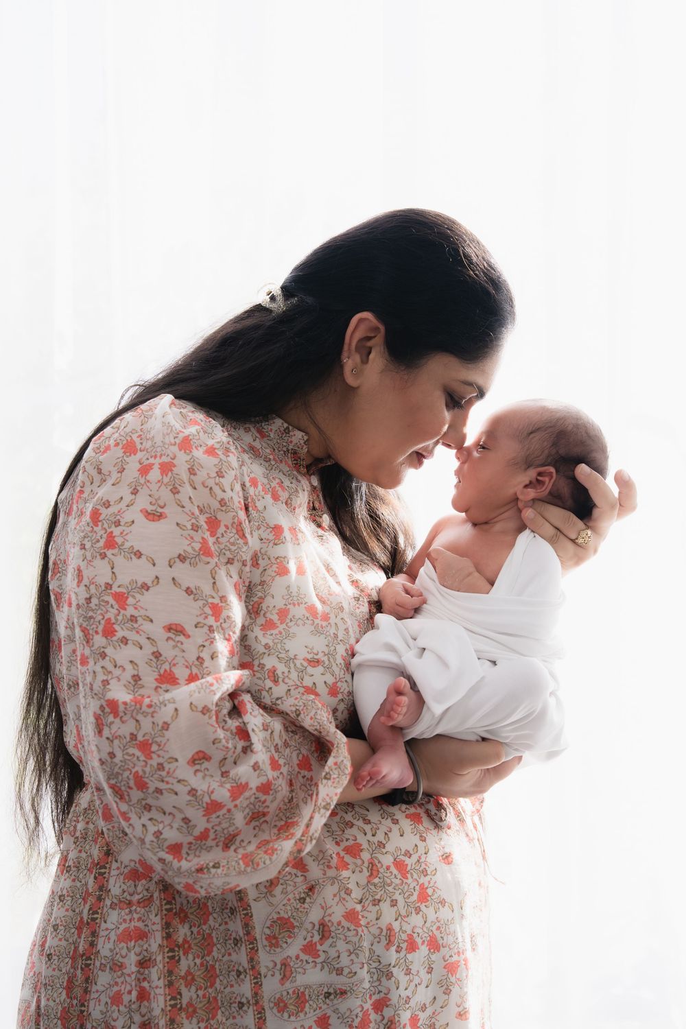 Three tender moments captured between parent and newborn baby in floral dress against white background.