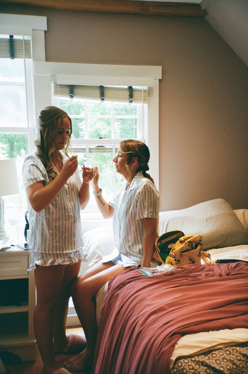 Four sequential photos show friends sharing drinks and laughing while sitting on a bed with pink bedding.