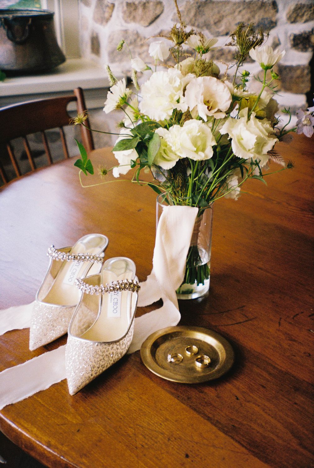 Elegant white bridal shoes and floral arrangements displayed on a wooden table.