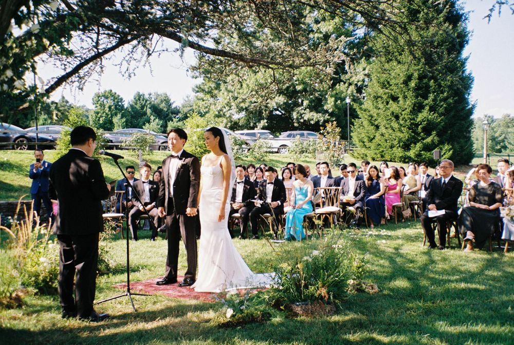 An outdoor wedding ceremony with guests seated on a grassy lawn.