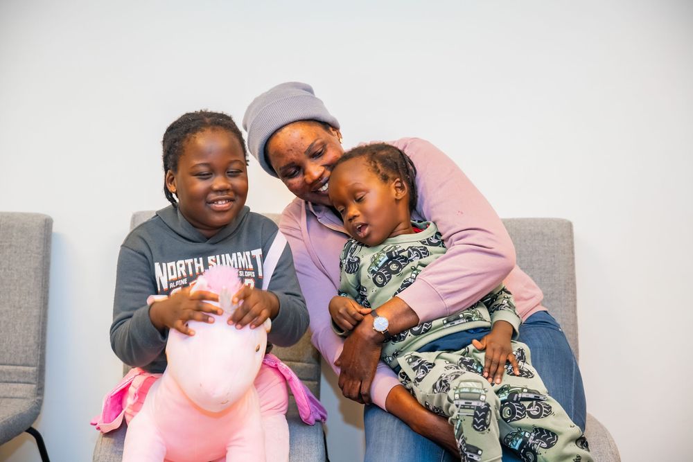 A family shares a joyful moment together on a gray couch while holding a pink plush toy.