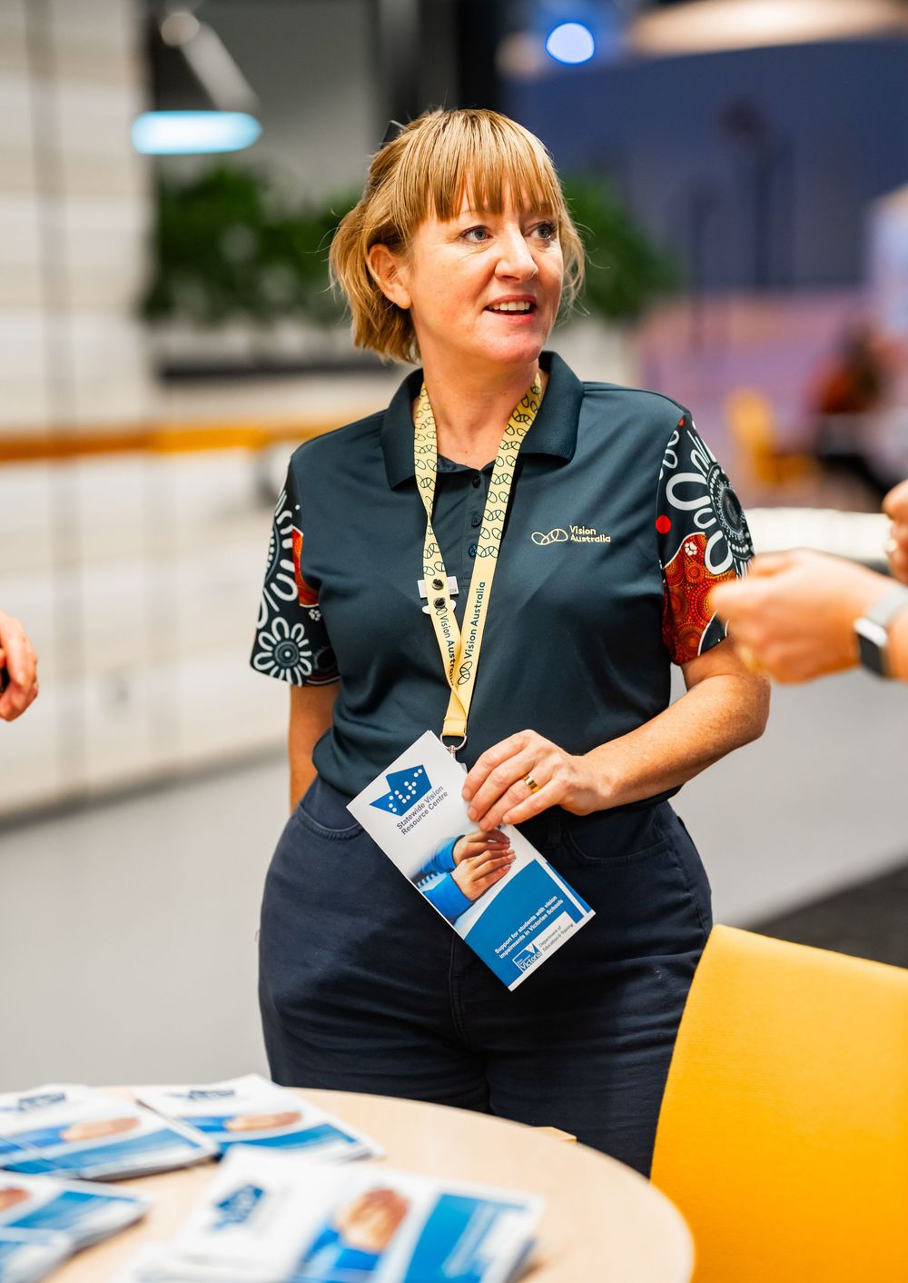 A person in a navy uniform smiles while holding brochures at an informational event.