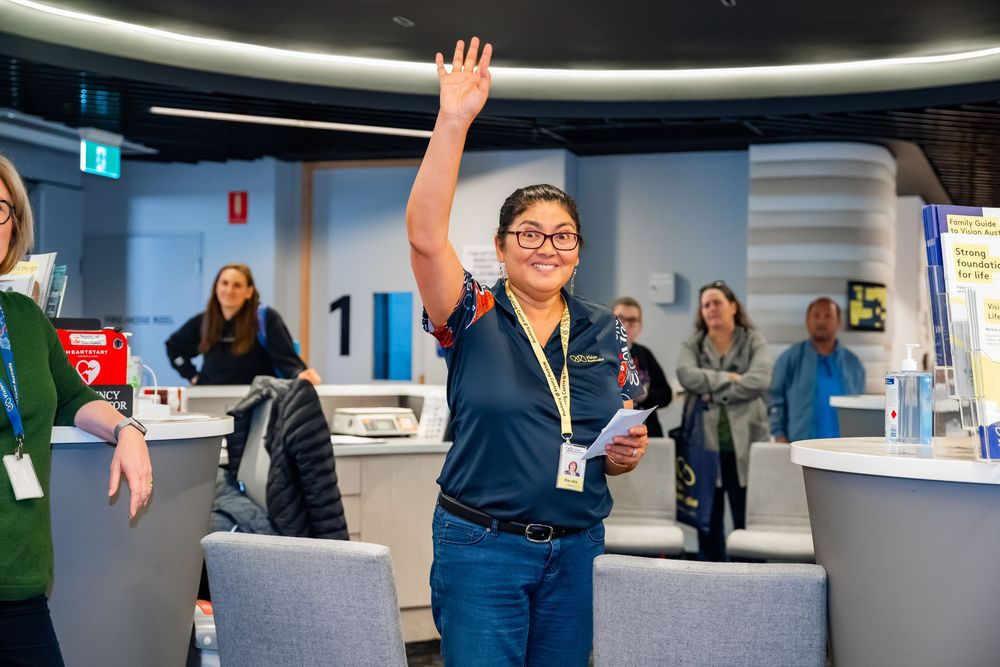 A person in business attire raises their hand enthusiastically during a meeting in a bright modern office space.