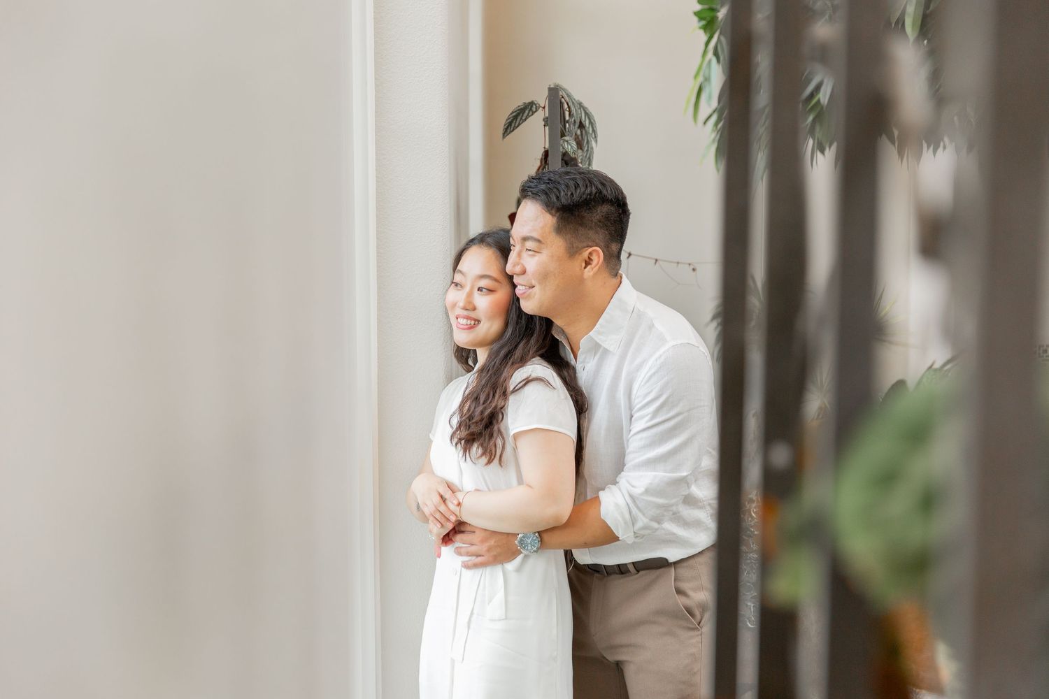 A couple shares an intimate moment on a wooden bench in a garden setting with pink flowers and water in the background.
