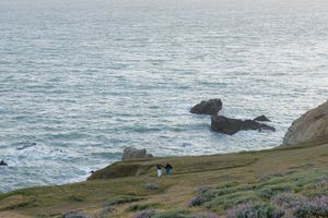 Dramatic oceanside cliffs and shoreline with waves crashing against rocks at sunset.