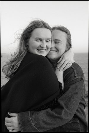 A black and white portrait of two people embracing and laughing together outdoors.
