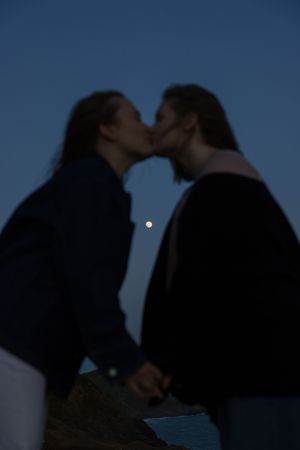 Silhouettes of a couple against a dark blue twilight sky with a small moon visible in the distance.
