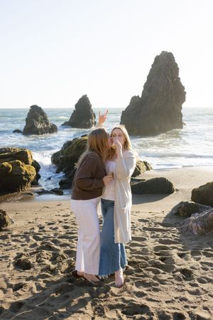 Romantic couple embracing while looking out at the rocky coastal shoreline at sunset with waves crashing against sea stacks.