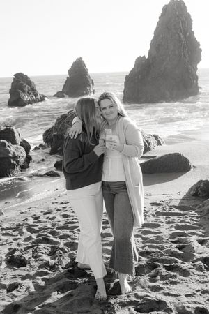 Two people stand together on a beach with dramatic rock formations and ocean waves in the black and white scene.