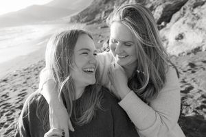 Two friends sharing a candid laughing moment together on a beach in black and white.