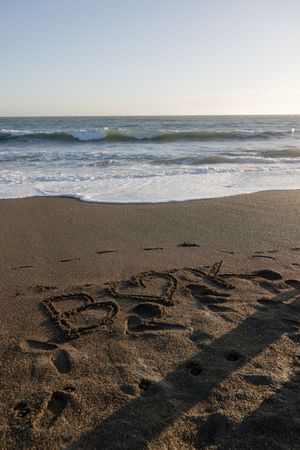 The word 'Beach' written in the sand with ocean waves and blue sky in the background.
