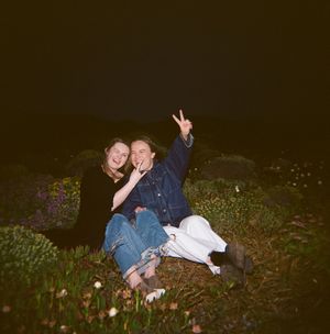 Two people sitting on grassy hillside at night making peace signs.